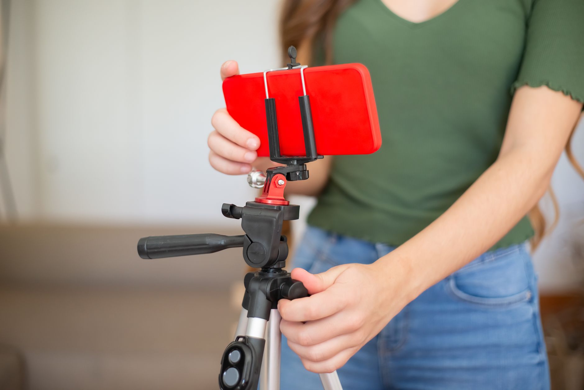 A person in a green top tightening a tripod while a red smartphone is clamped on top, held in landscape.